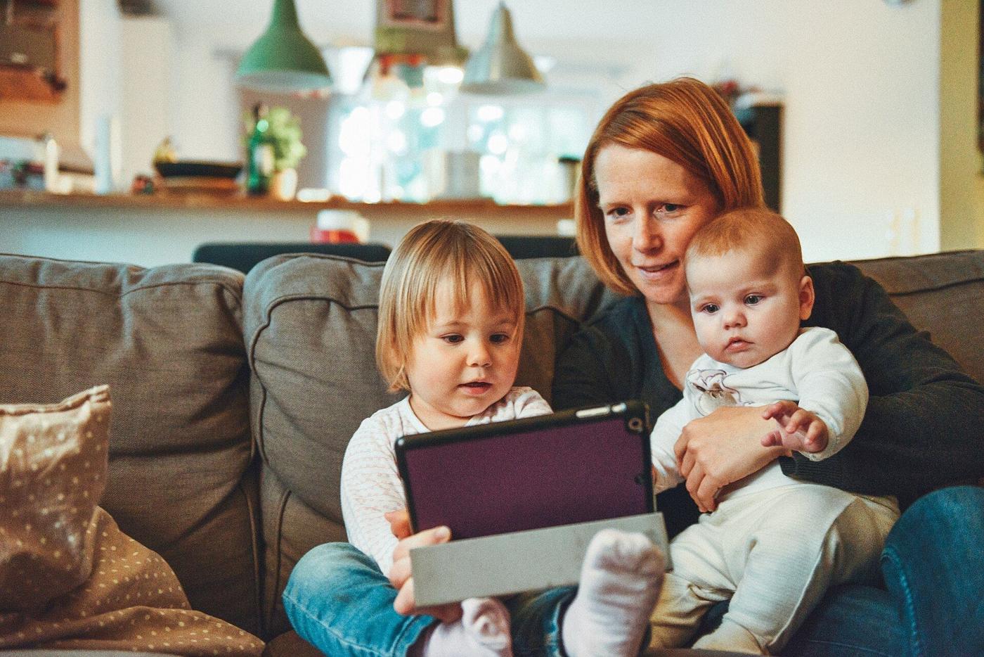A mother and her two young children looking at photos on a tablet on the sofa at home